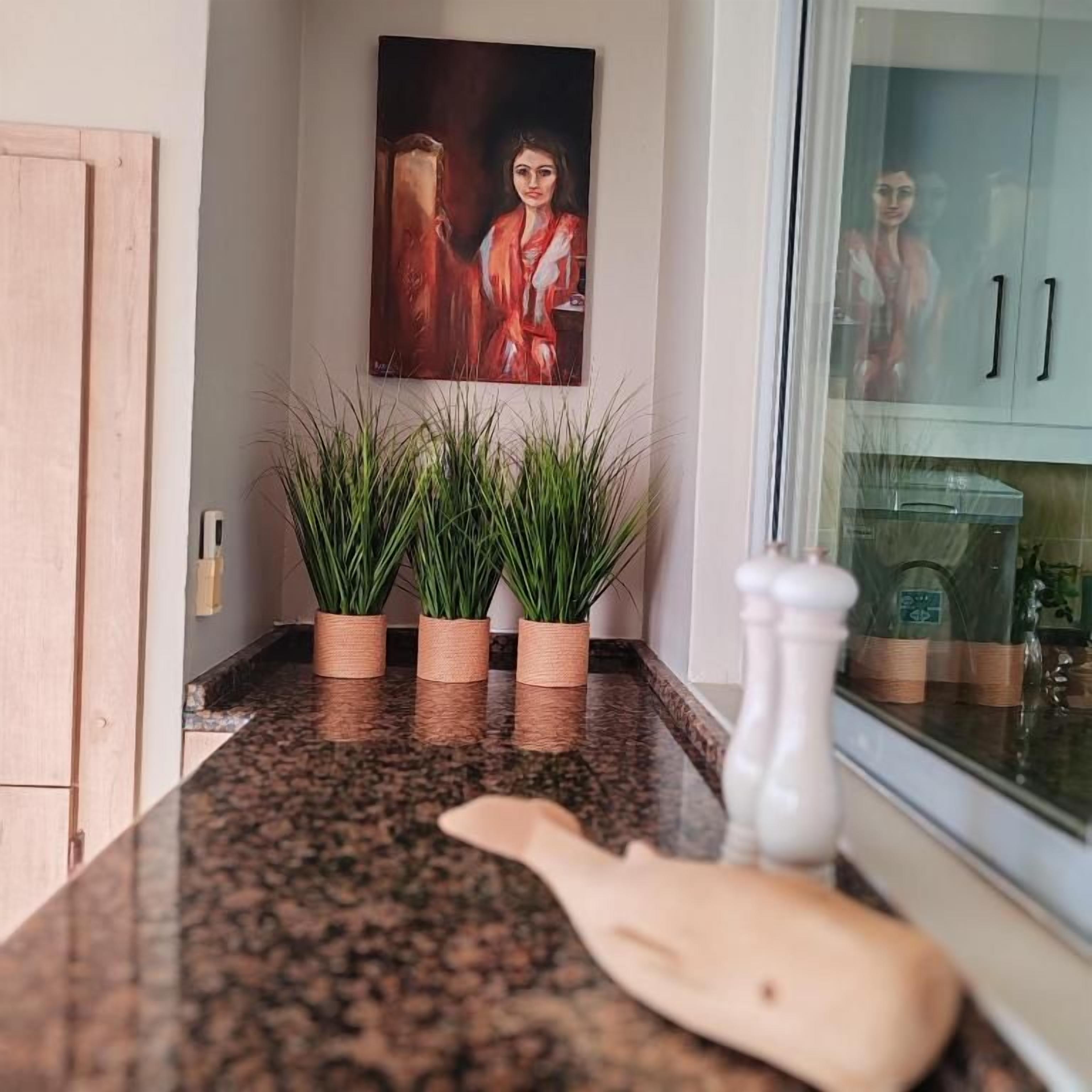 A kitchen counter with a granite surface, three potted plants, a salt shaker, and a wooden cutting board.