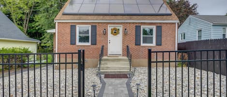 A two-story brick house with a front entrance, a solar panel roof, and a gravel driveway.