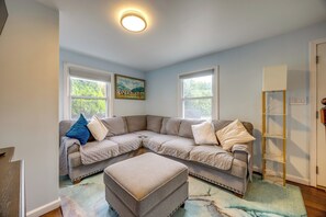 Ein Wohnzimmer mit einem Ecksofa, passendem Hocker, einem Bild an der Wand und einer Deckenleuchte.