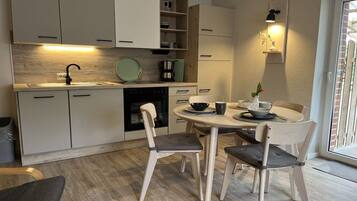 Une cuisine moderne avec un coin repas, dotée de meubles en bois clair, d’une table ronde et d’un four encastré.