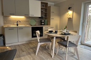 A modern kitchen with a dining area, featuring light wood cabinetry, a round dining table, and a built-in oven.