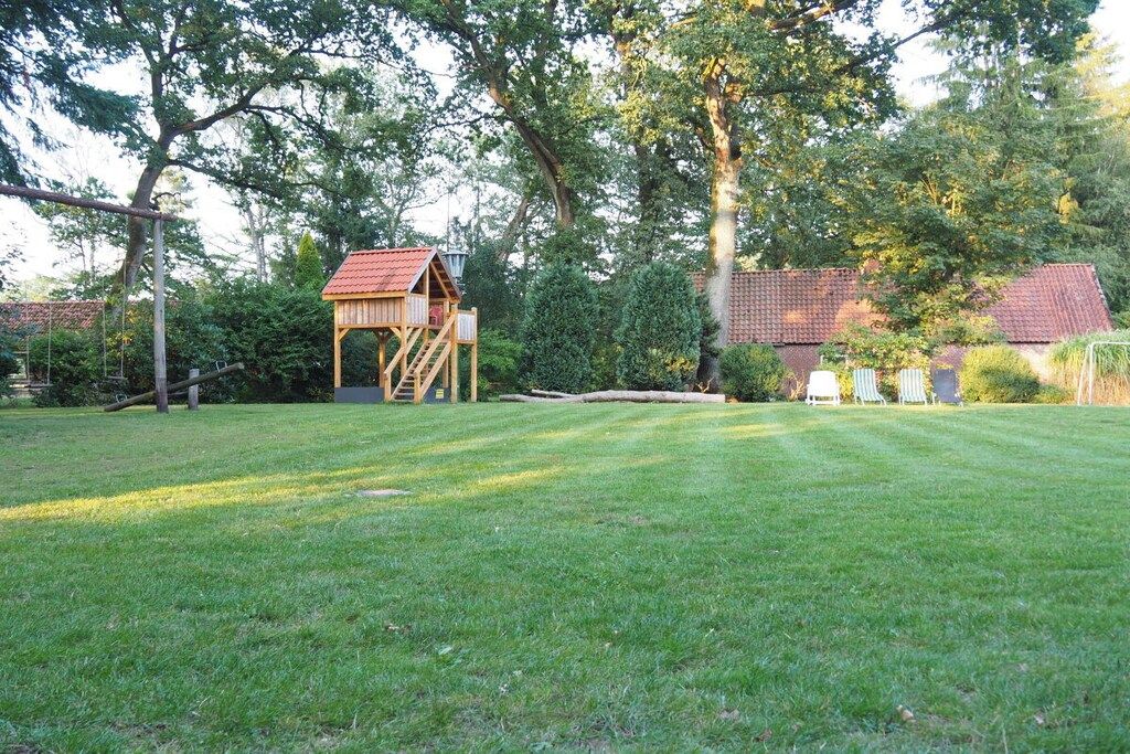 A grassy outdoor area with a wooden play structure and a house in the background.