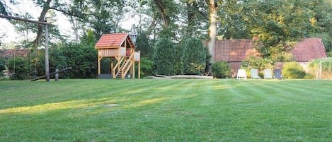 A grassy outdoor area with a wooden play structure and a house in the background.