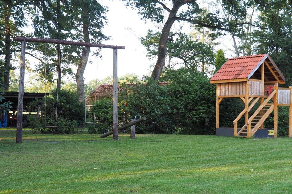 A playground with swings, a slide, and a wooden playhouse with a red roof.