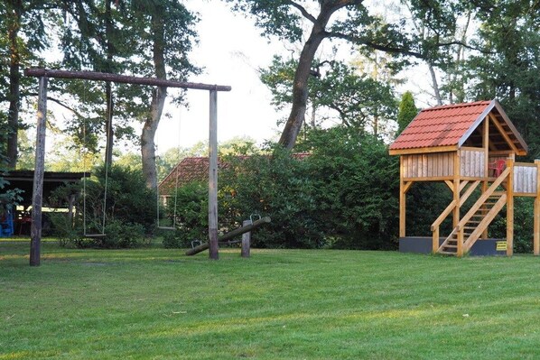 A playground with swings, a slide, and a wooden playhouse with a red roof.