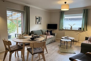 A living room with a sofa, a television, a dining table with chairs, and a window with curtains.