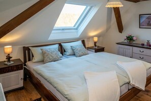Un dormitorio con tragaluz, una cama con almohadas, mesitas de noche con lámparas y un aparador con un florero.