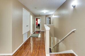 A hallway with a wooden floor, a white door, and a staircase with a handrail. - 9BR Group Getaway Outside Fort Worth (Justin)