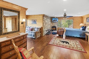 A log cabin interior with a fireplace, a bed, a sofa, a wooden dresser, and a mirror. - Luxury Castle Glen Estate 4 Bedroom! Game Room! Walking Distance to Lake and Trails! (Big Bear Lake)