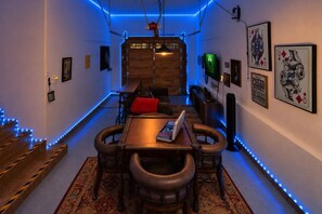A narrow hallway with a dining area featuring a wooden table and leather chairs, blue LED lights, and poker night posters. - Luxury Castle Glen Estate 4 Bedroom! Game Room! Walking Distance to Lake and Trails! (Big Bear Lake)