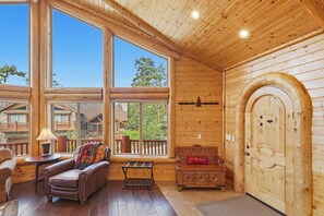 L’intérieur d’une cabane avec une grande fenêtre, une porte en bois, un banc et un canapé.