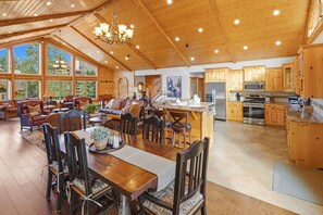 Une cuisine spacieuse avec des meubles en bois, un coin repas doté d’une grande table et un salon avec des canapés en cuir.