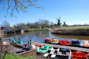 Ein Fluss mit vertäuten Booten, einer Windmühle und einer Brücke.