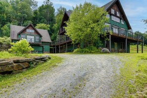 Ein rustikales Blockhaus mit Kiesweg, umgeben von üppiger Vegetation und Bäumen.