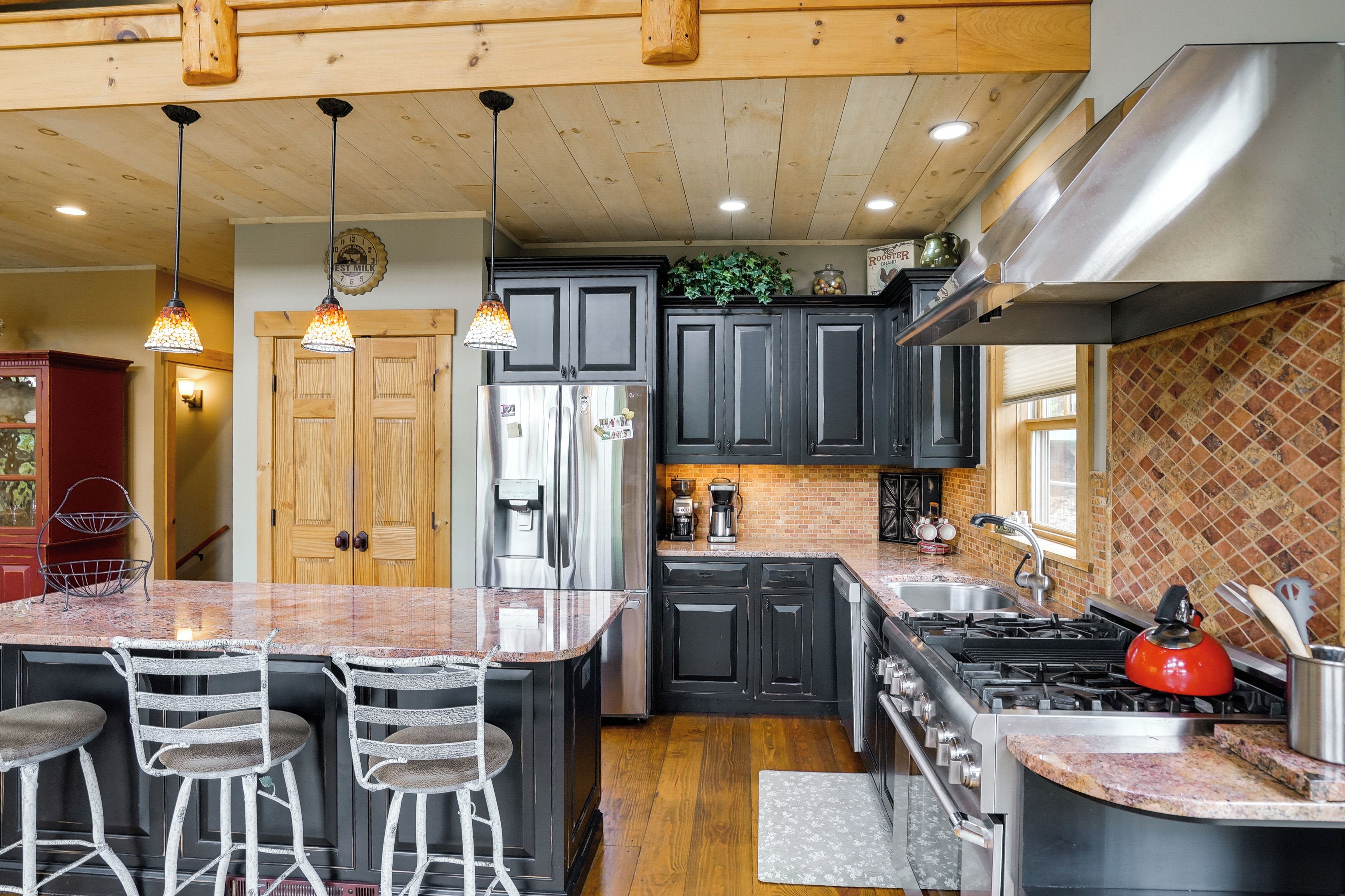 Una cocina con una isla central, taburetes de bar, un refrigerador, una estufa y un lavaplatos.