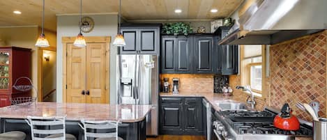 Una cocina con una isla central, taburetes de bar, un refrigerador, una estufa y un lavaplatos.