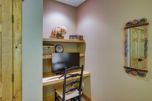 Quarto com escrivaninha de madeira, cadeira, televisão, relógio e espelho decorativo na parede.
