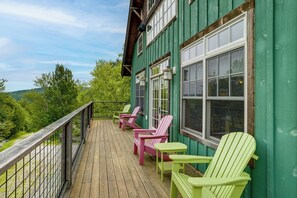 Um deck de madeira com cadeiras Adirondack e vista para um morro arborizado.