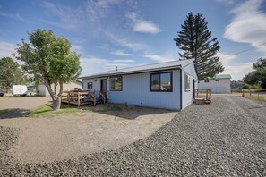A single-story house with a gravel driveway, a wooden deck, and a large tree in front.