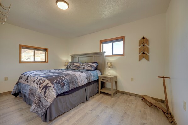 A bedroom with a bed, bedside table, lamp, and a wall-mounted wooden object.