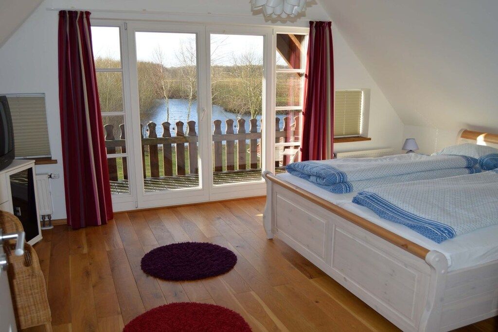A bedroom with a bed, a television, and a view of a lake through large glass doors.