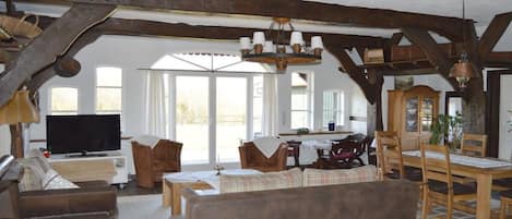 A spacious living room with a television, wooden furniture, and a dining area with a table and chairs.