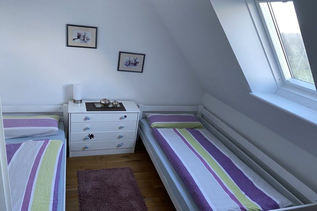 A bedroom with two single beds, a white dresser with drawers, a small table with a lamp, and two framed pictures on the wall.