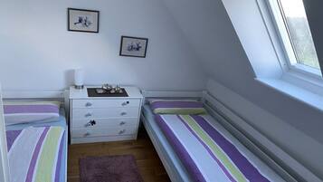 A bedroom with two single beds, a white dresser with drawers, a small table with a lamp, and two framed pictures on the wall.