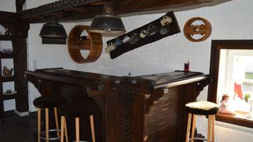 A rustic bar area with wooden stools, a bar counter, and various kitchen utensils hanging on the wall.