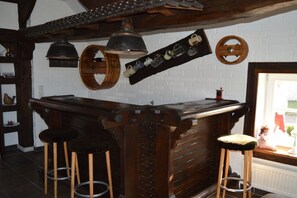 Ein rustikaler Barbereich mit Holzhockern, einer Bar und verschiedenen Küchenutensilien, die an der Wand hängen.