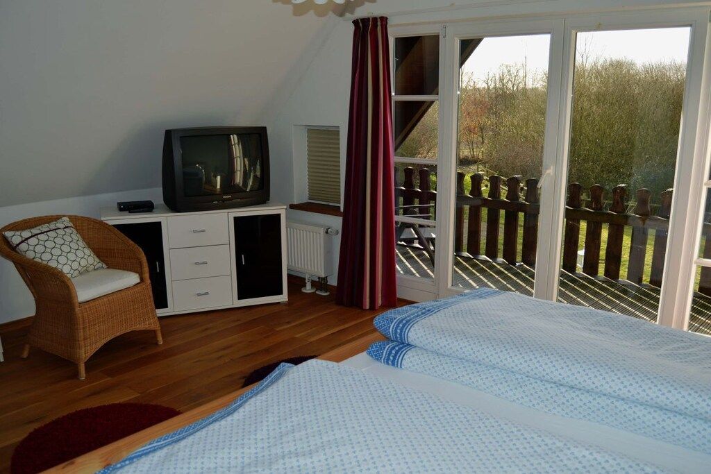 A bedroom with a bed, a television, a chair, and a sliding glass door leading to a balcony.
