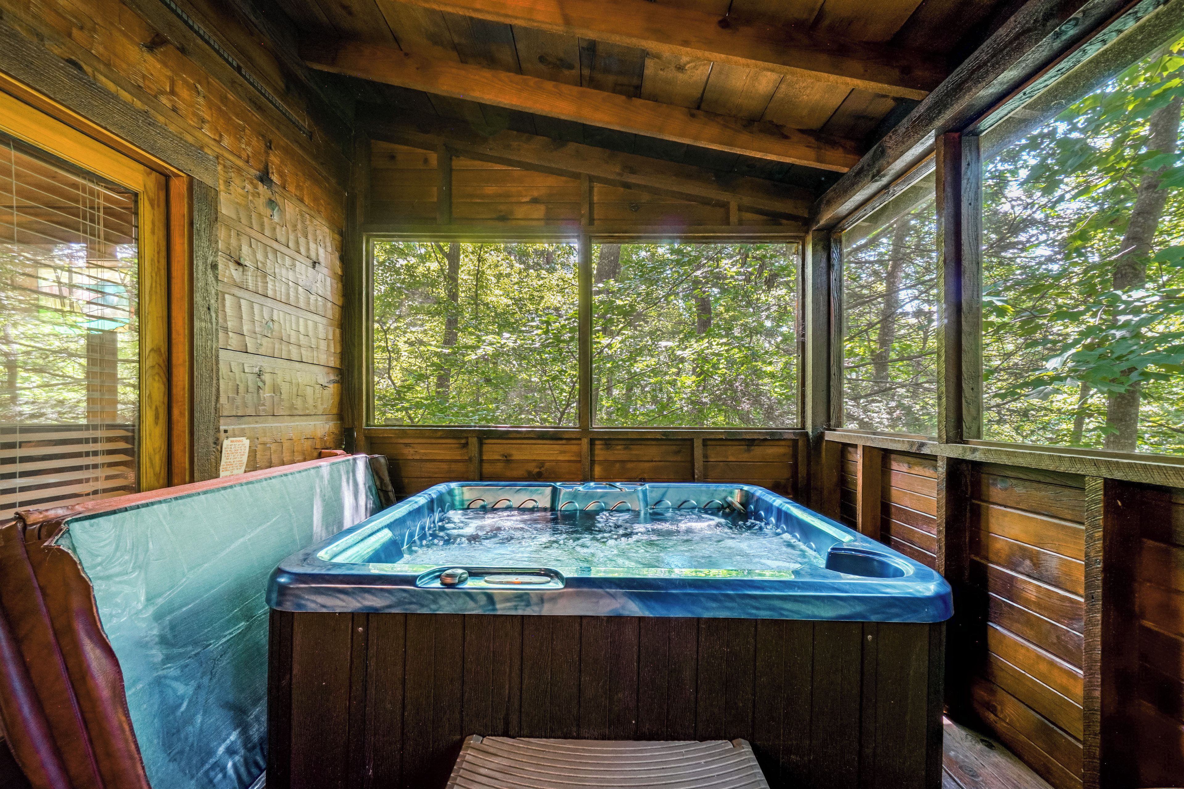 A hot tub in a wooden cabin with a view of a forest through large windows.