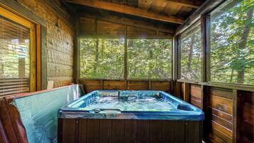 A hot tub in a wooden cabin with a view of a forest through large windows.