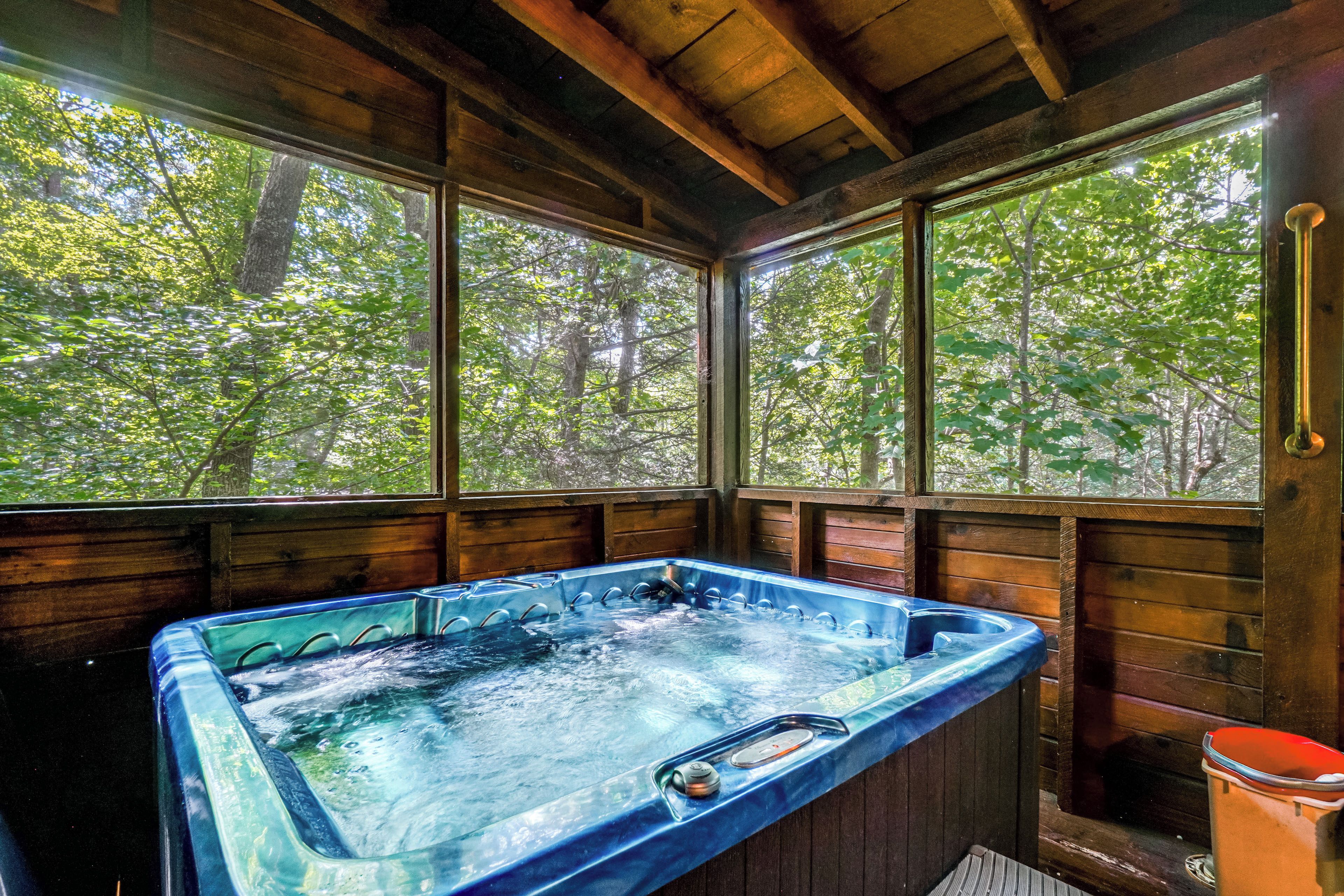 Une cabane en bois dotée d’un bain à remous et de grandes fenêtres donnant sur une forêt.