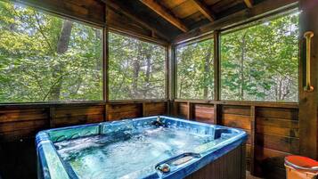 Une cabane en bois dotée d’un bain à remous et de grandes fenêtres donnant sur une forêt.