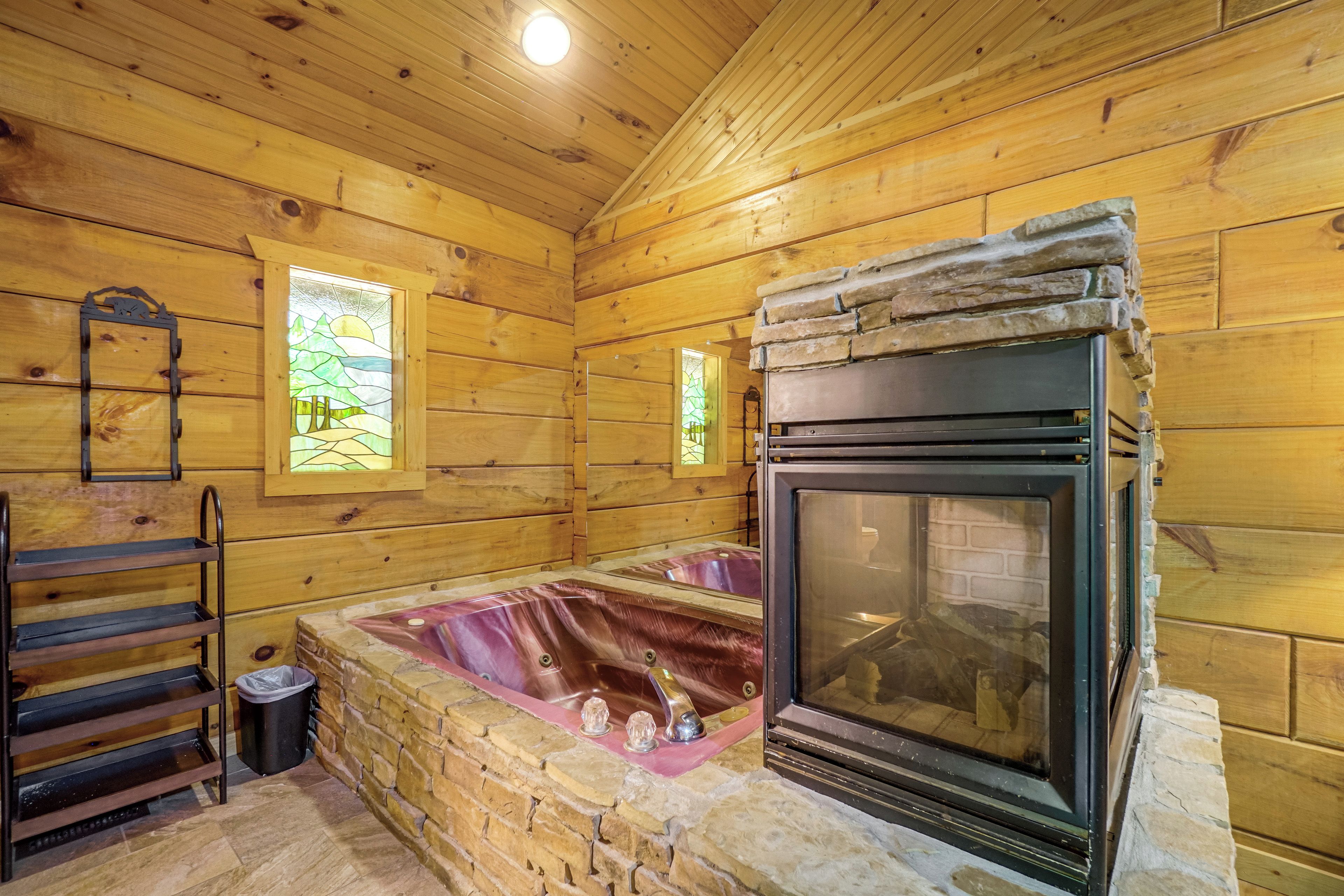 A cozy cabin interior with a stone fireplace, wooden walls, and a window with a view of trees.
