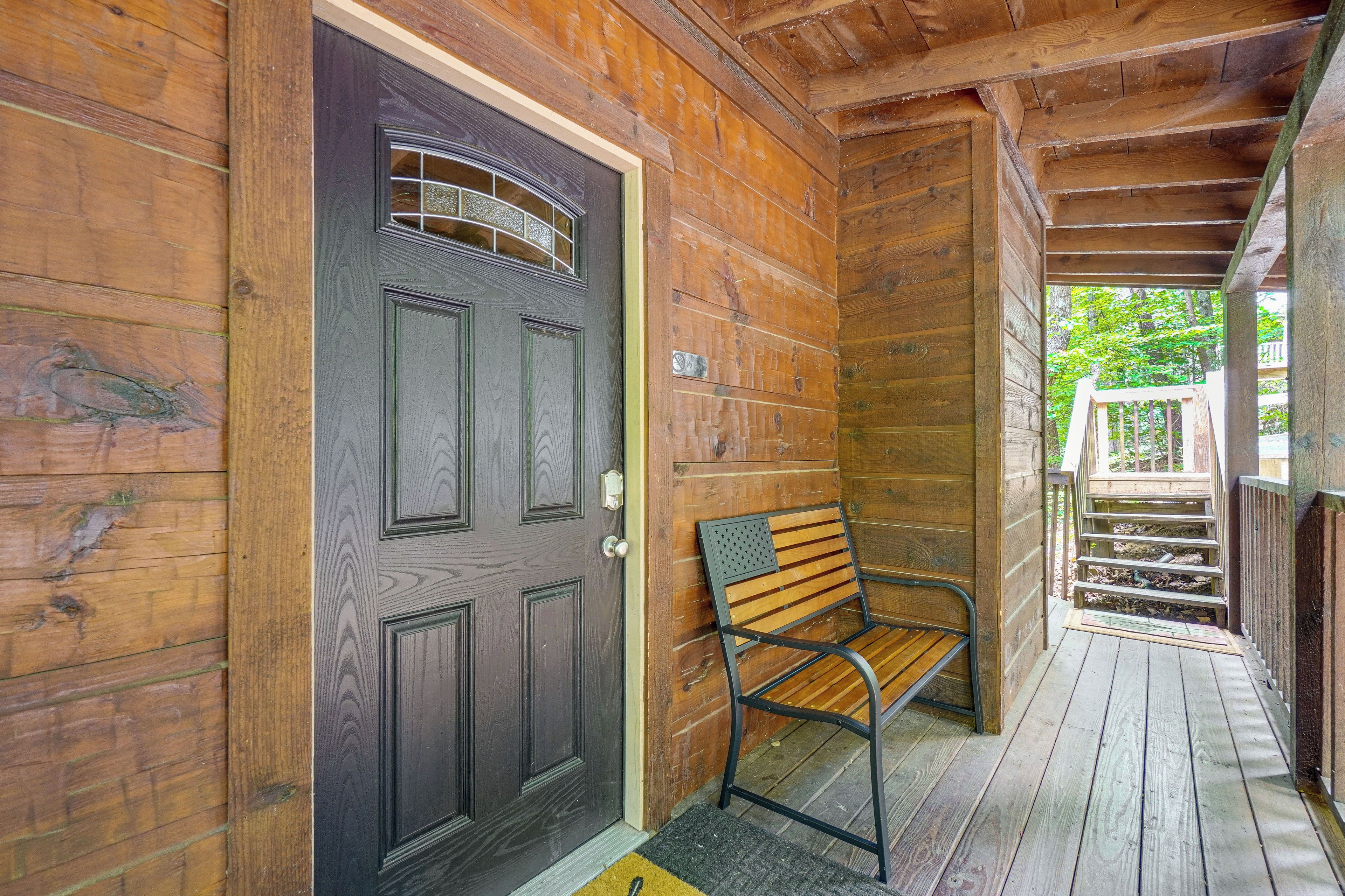 A wooden cabin with a dark door, a bench, and a wooden staircase leading to a deck.