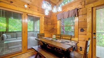 A wooden cabin interior with a dining table, benches, and a window with blinds.