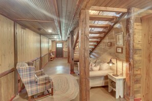 A wooden interior with a staircase, a plaid chair, a round rug, and a lamp.