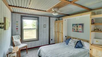 A bedroom with a single bed, a wooden chair, a window, and a bookshelf.