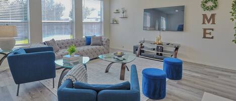 A modern living room with a sectional sofa, a glass coffee table, and a TV mounted on the wall.