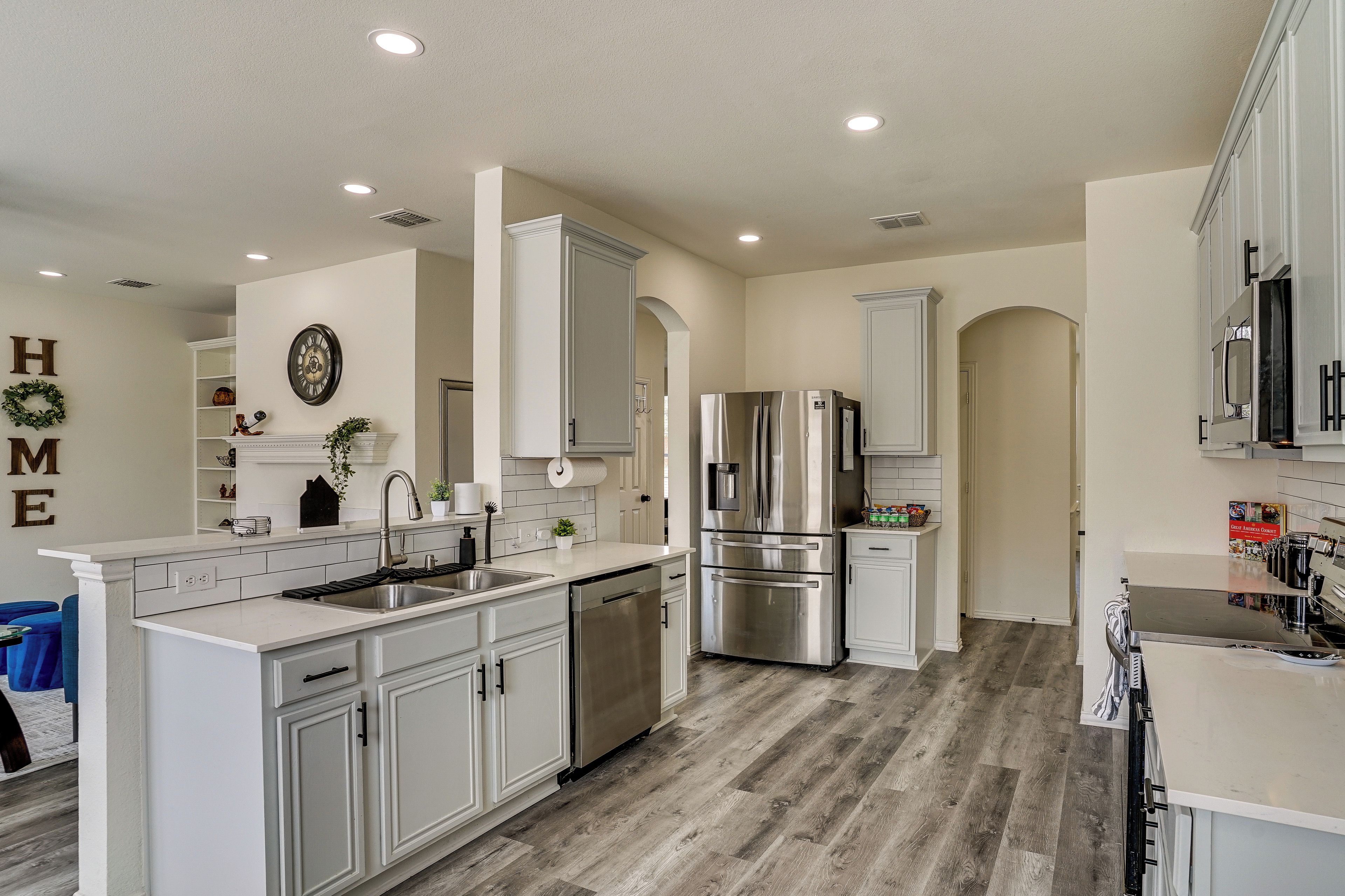 A modern kitchen with white cabinetry, stainless steel appliances, and a wooden floor.
