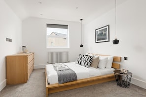 A modern bedroom with a bed, bedside table, dresser, window, and artwork. - New! Charming 2BR | Parking | Brockley (Greater London)