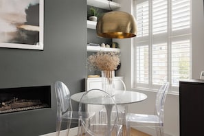 A modern dining area with a round table and clear chairs, a pendant light, and a fireplace. - New! Charming 2BR | Parking | Brockley (Greater London)