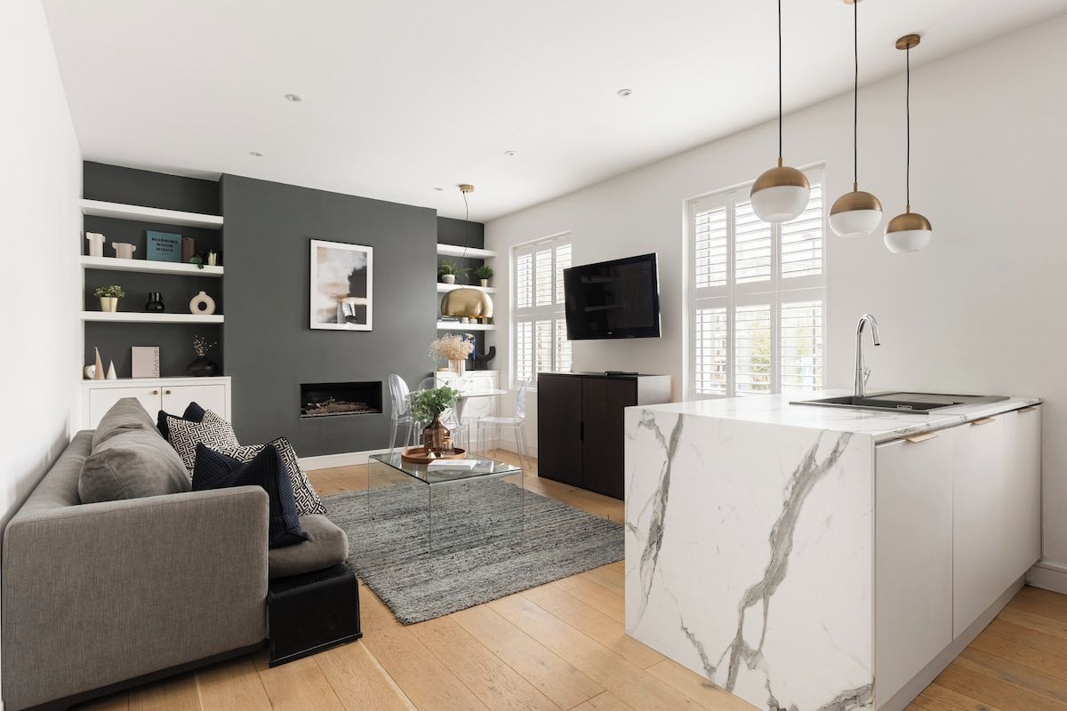 A modern kitchen with a marble island, built-in shelving, and pendant lighting.
