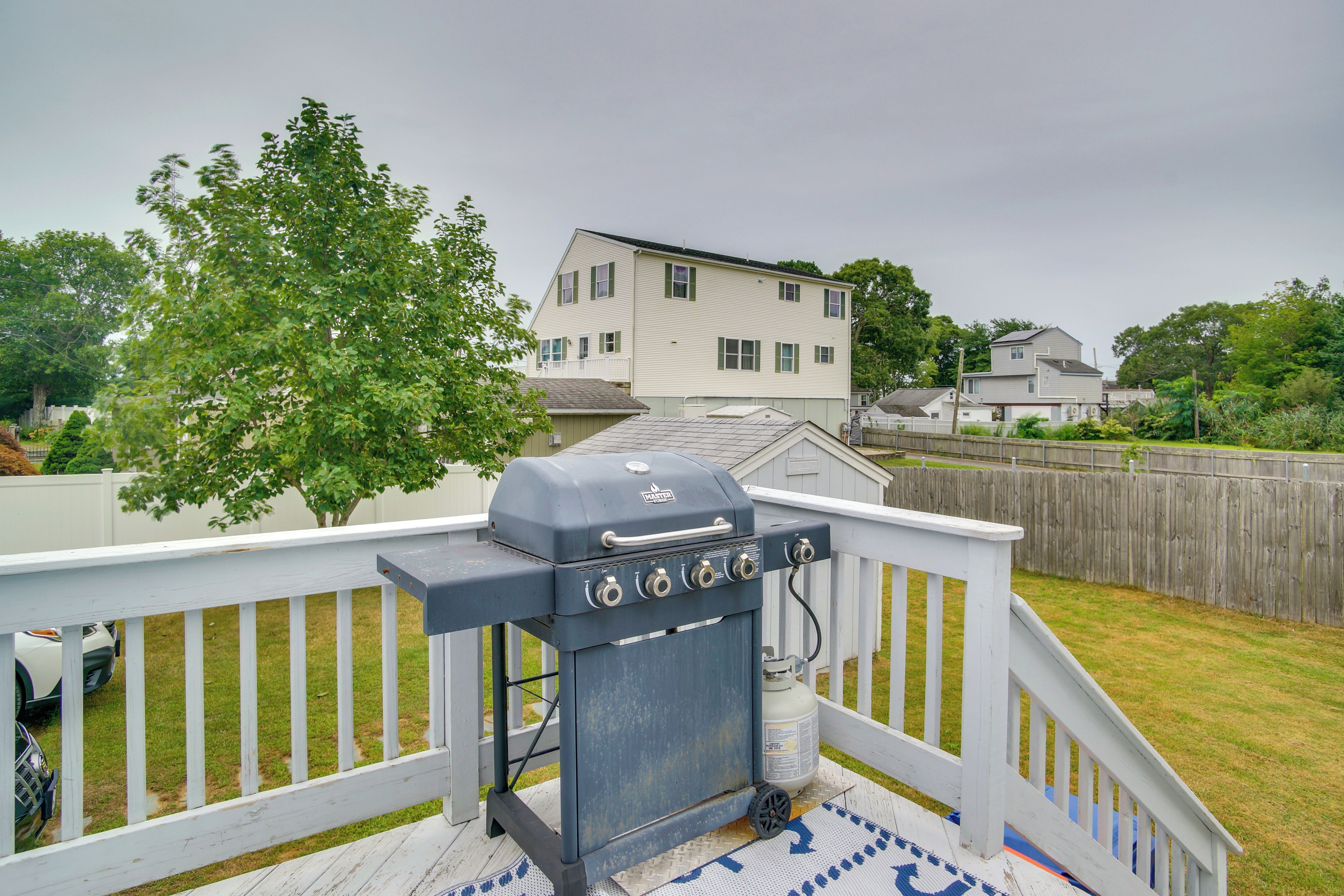 A backyard with a barbecue grill on a deck, surrounded by a wooden fence and a house in the background.