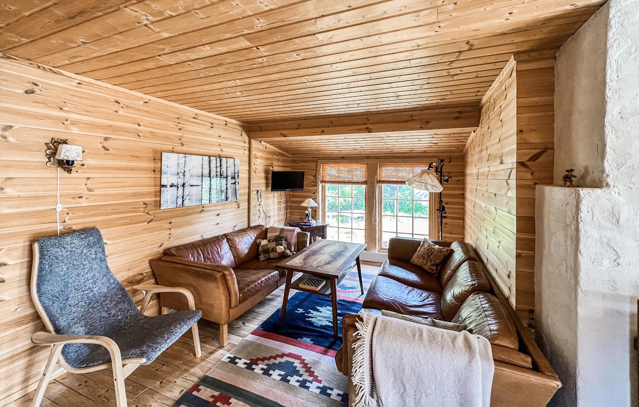A wooden interior with a sofa, chairs, a table, and a television.