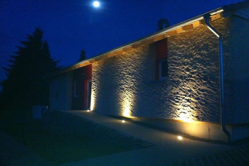 Edifici amb façana de pedra i porta vermella, il·luminat amb il·luminació exterior.