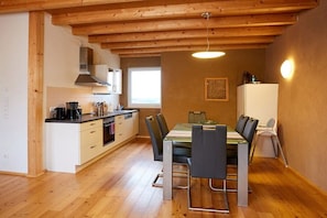 A compact kitchen with wooden beams, a dining table with chairs, and a refrigerator. - living in a straw house (Gillenfeld)