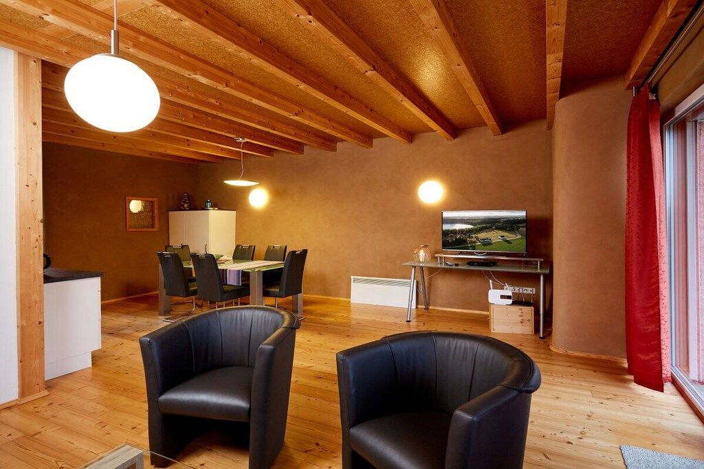 Une pièce avec un plafond en bois, un coin repas avec des chaises et une table, un téléviseur et une fenêtre avec des rideaux.